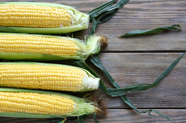 corn cob and green leaves on wooden background