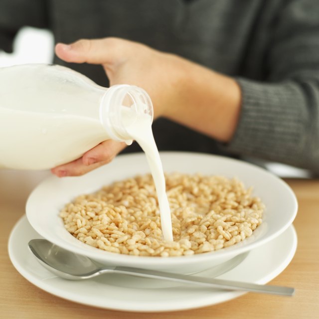 person pouring milk from a bottle into a bowl of cereal