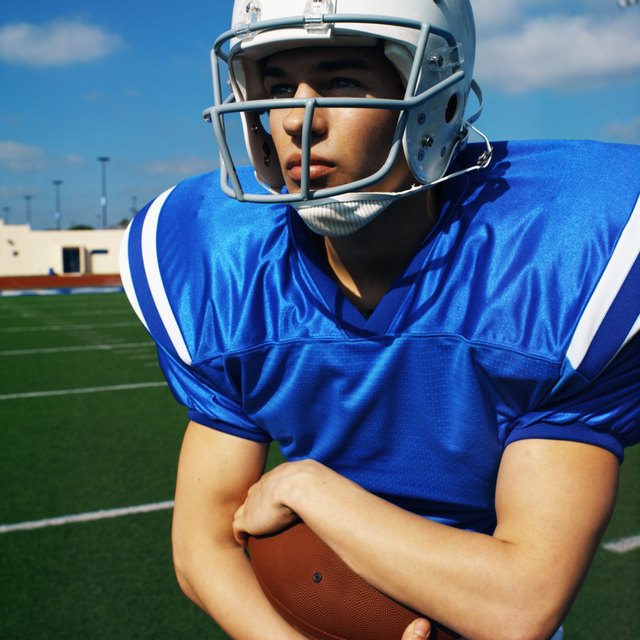 American football player (16-20) holding football looking into the distance