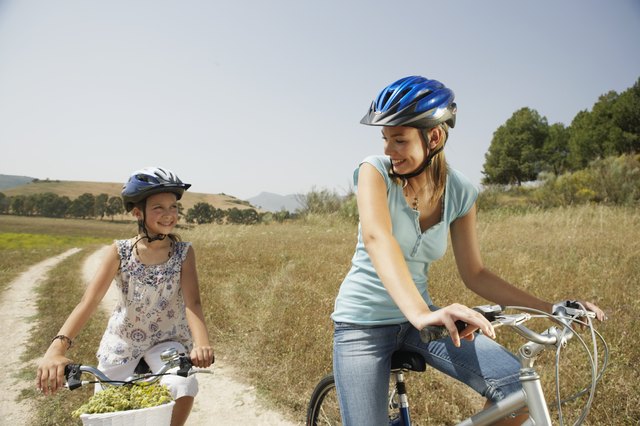 Mother and daughter (9-11) cycling, smiling at each other