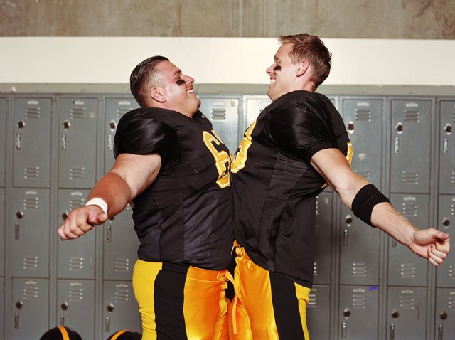 Football players bumping chests in locker room, side view