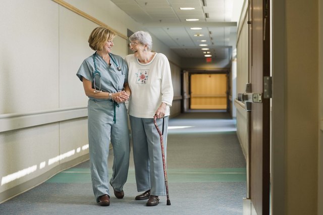 Nurse helping elderly woman walk down hallway