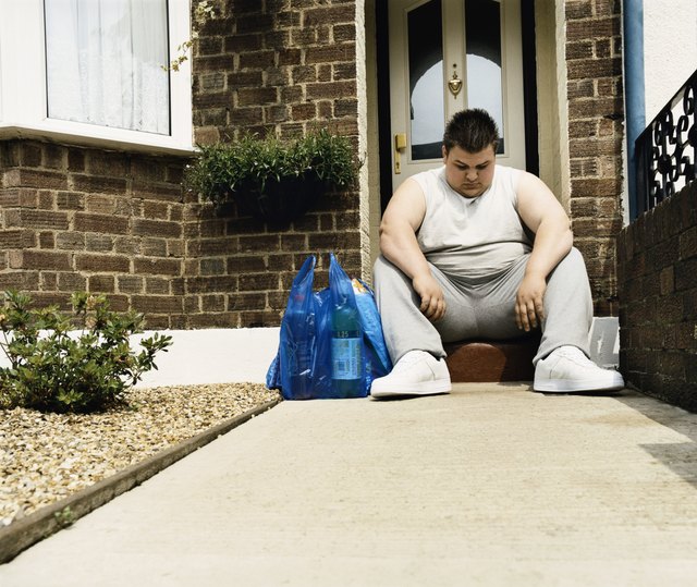 Overweight Man Sits Next to His Shopping on a Doorstep
