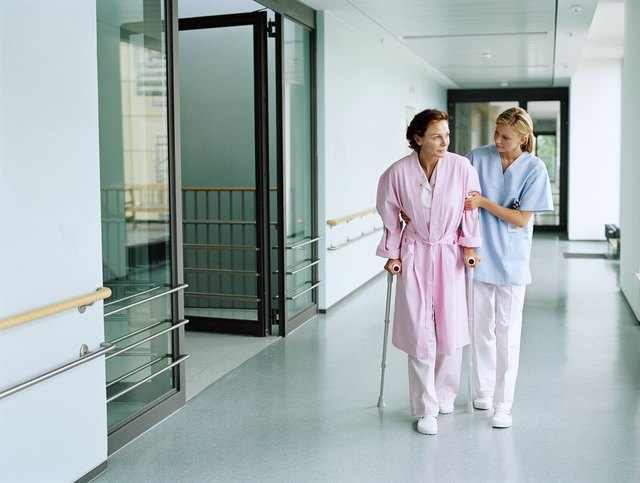 Nurse holding female patient using crutches in hospital corridor