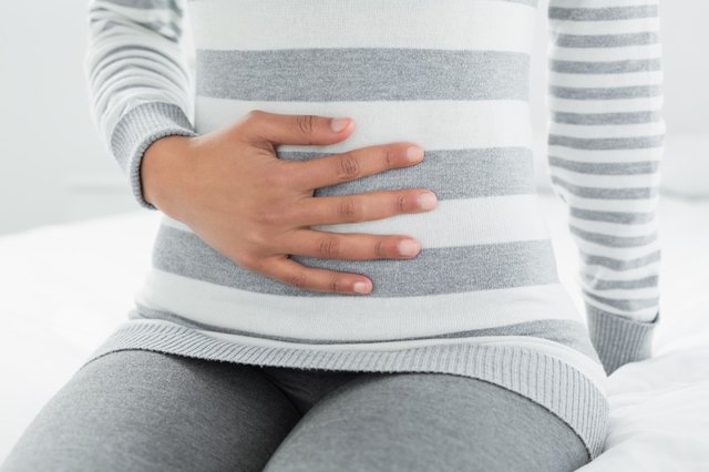Mid section of a woman with stomach pain sitting in bed