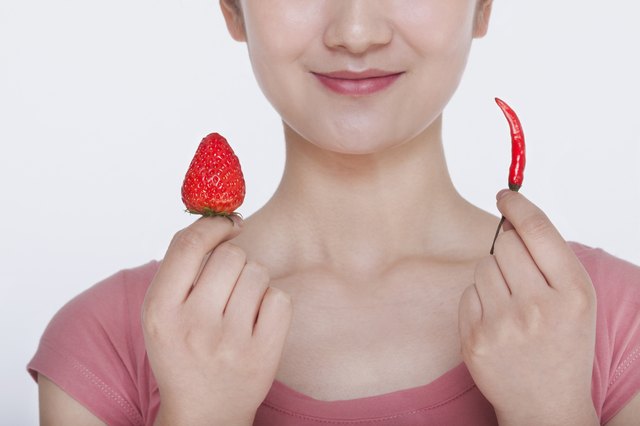 Young woman smiling and holding opposites, a strawberry and a chili pepper, in each hand