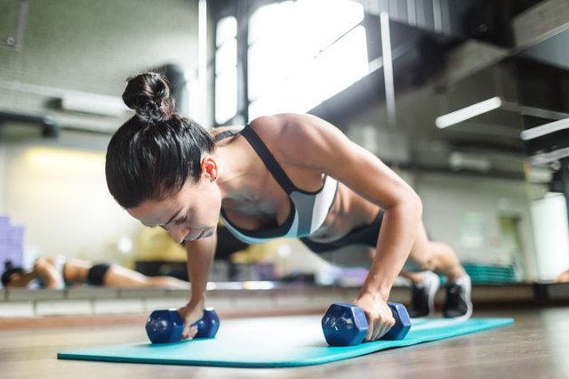 Muscular female doing planks with dumbbells