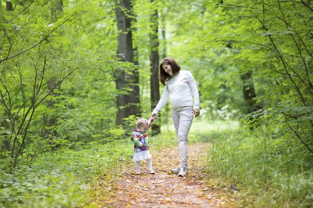 Beautiful pregnant woman and her baby daughter walking in park