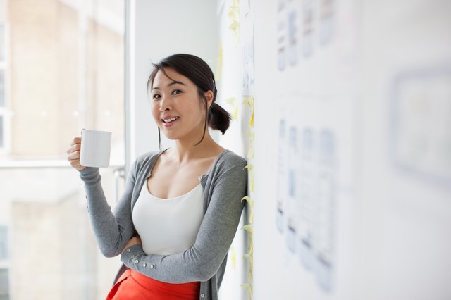 Smiling businesswoman leaning against whiteboard and drinking coffee