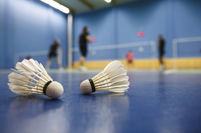 badminton courts with players competing; shuttlecocks in the foreground