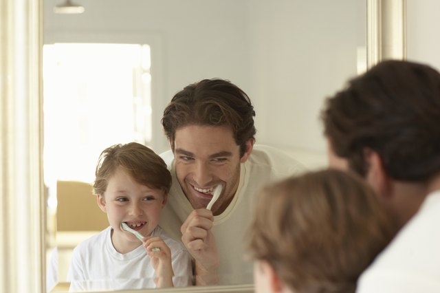 Father and son (5-7) brushing teeth, looking at reflections in mirror