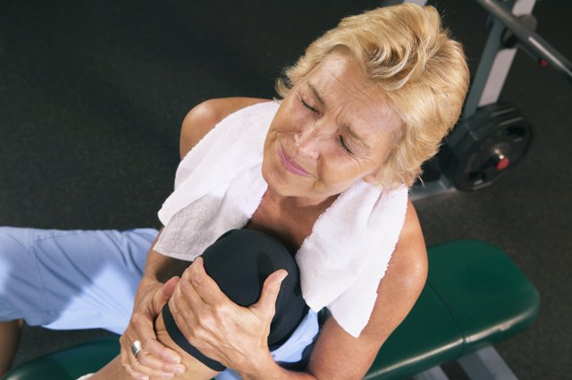 Mature woman in gym holding knee, eyes closed, overhead view