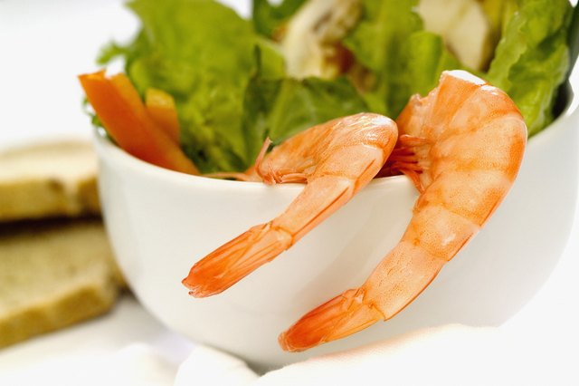 Two shrimp with tails on hanging on the side of a bowl of salad, close-up, selective focus