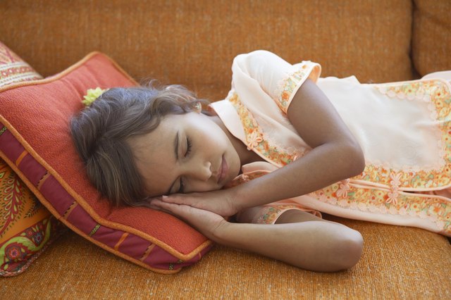 Girl (7-9) sleeping on sofa, resting head on cushion, close-up