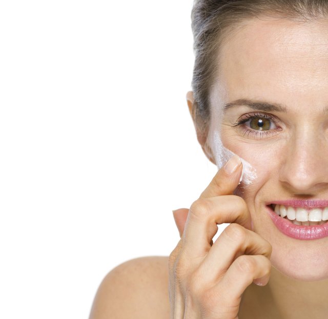 Happy young woman applying creme on cheek. Closeup