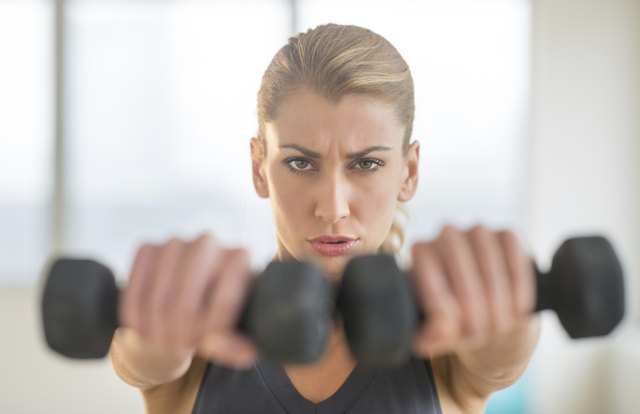 Dedicated Woman Lifting Dumbbells At Health Club