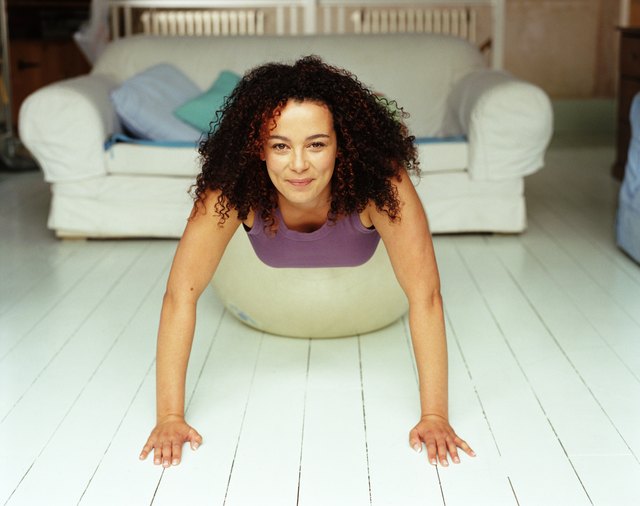 Woman doing push-ups on fitness ball in living room, smiling, portrait