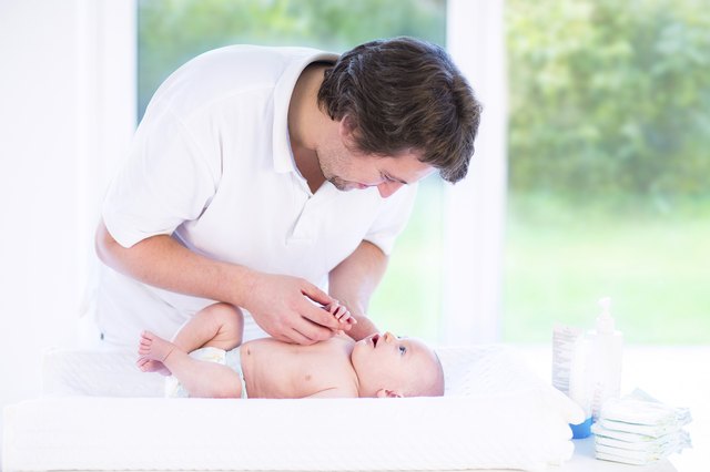 Young father talking to newborn baby relaxing on changing table