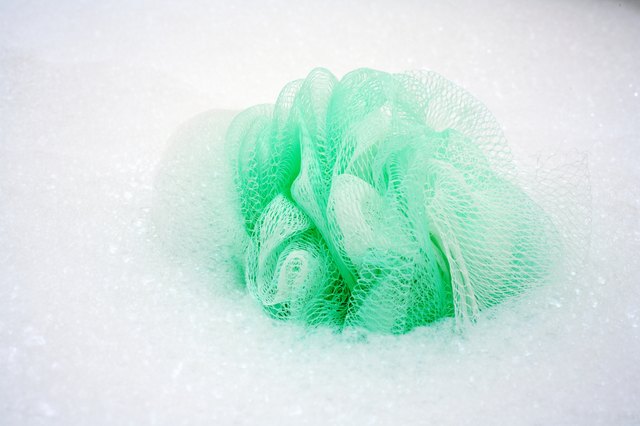 Spa elements, Green loofa with lots of bubbles in bathtub.