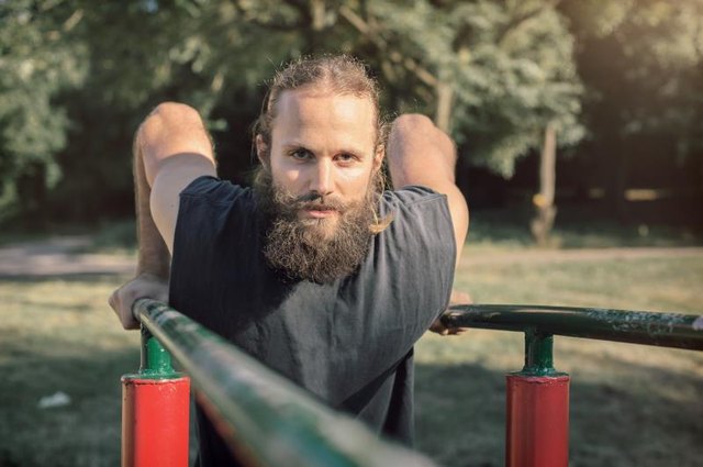 Training outdoors. Man doing biceps and triceps dips training on horizontal bars in the sport park.