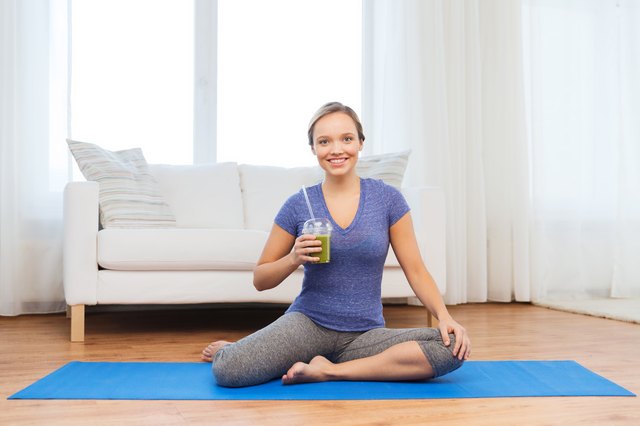 happy woman with smoothie sitting on mat at home