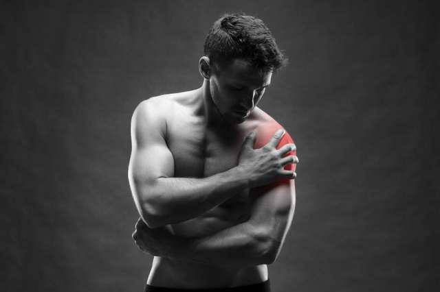 Pain in the shoulder. Muscular male body. Handsome bodybuilder posing on gray background. Black and white photo with red dot