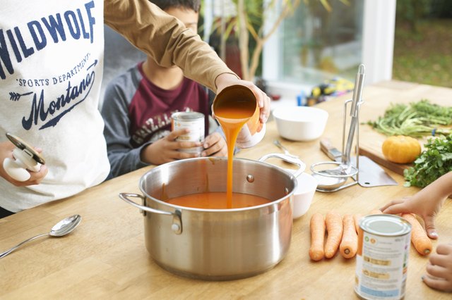 Cropped shot of boy pouring tin of tomato soup into saucepan