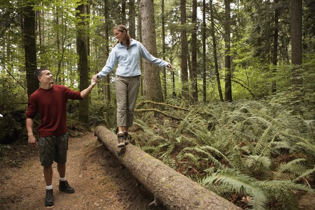 Man holding woman's hand as she walks across log in forest