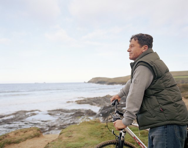 Mature man holding bicycle handle bars, overlooking sea, side view