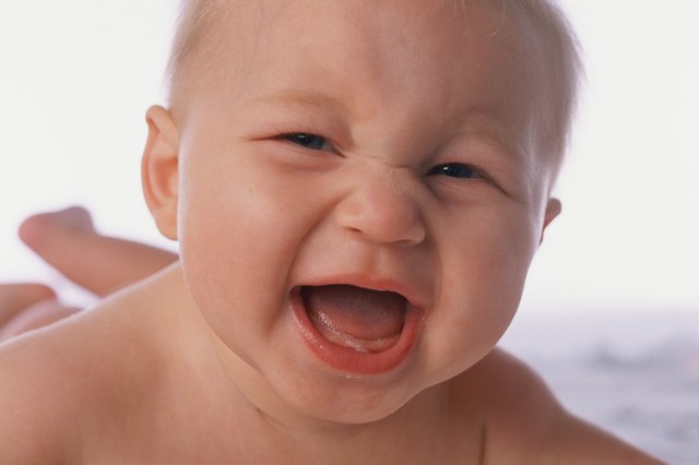 Close-up of baby laughing, lying on stomach on bed