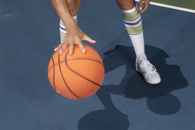 Woman standing dribbling basketball, low section, blurred motion