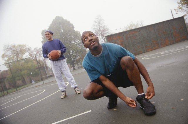 Young man lacing up basketball shoes on street court