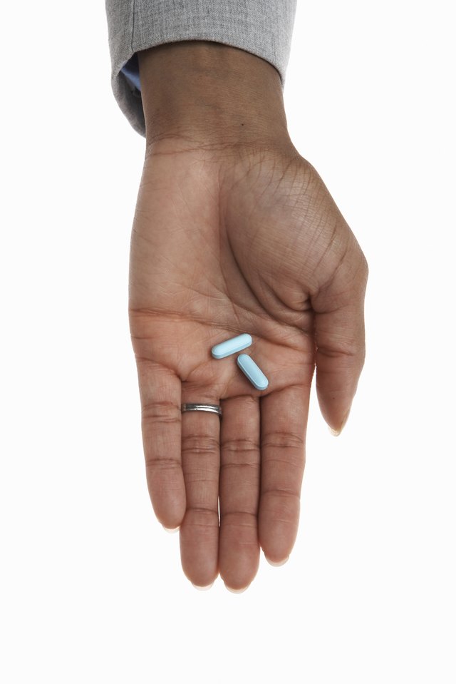 Young woman holding two pills, close-up of hand