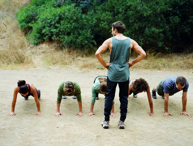 Man standing over group of people doing pushups, rear view