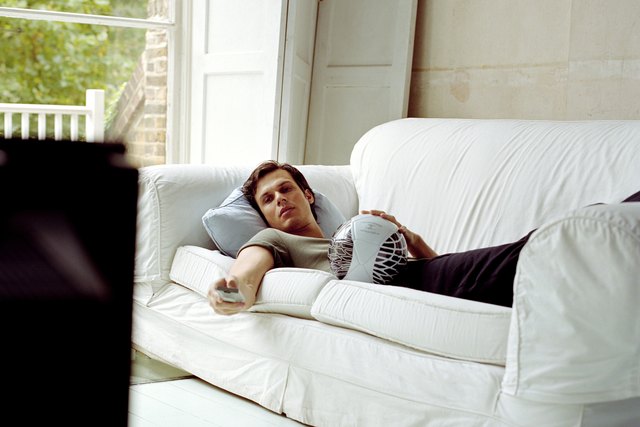 Man lying on sofa using television remote control