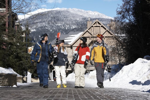 Four adults with skis and snowboards walking and talking