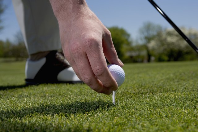 Close-up of a young man putting a golf ball on a tee