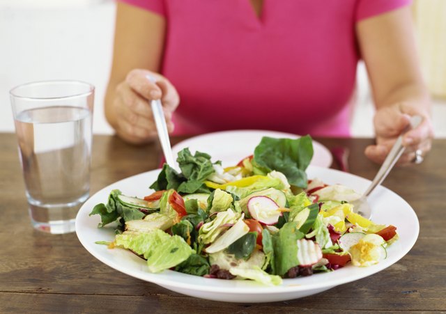 mid section view of a woman with a plate of salad on a table