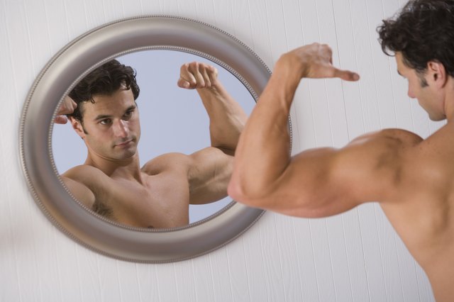 Muscular man looking in mirror and flexing arms