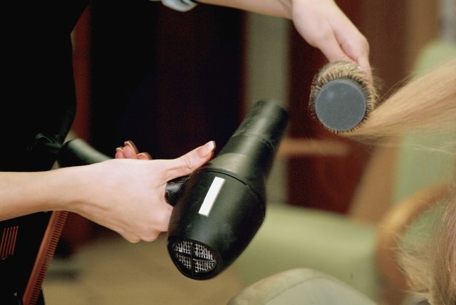 Close-up of a female hairdresser's hands styling a mid adult woman's hair