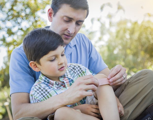 Loving Father Puts Bandage on Knee of Young Son