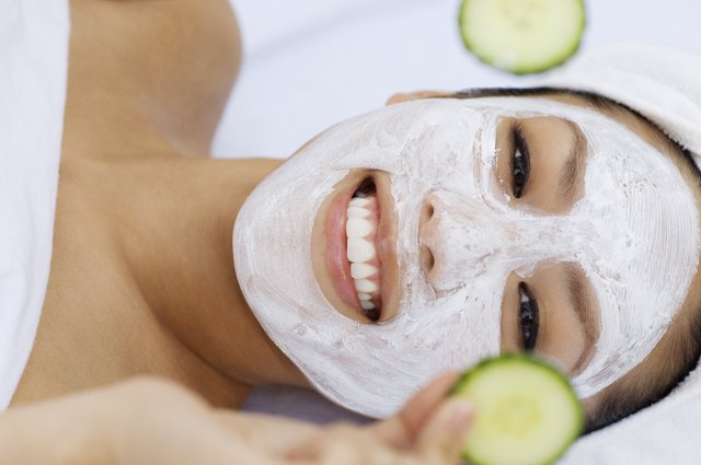 Young woman having facial treatment, holding cucumbers, portrait