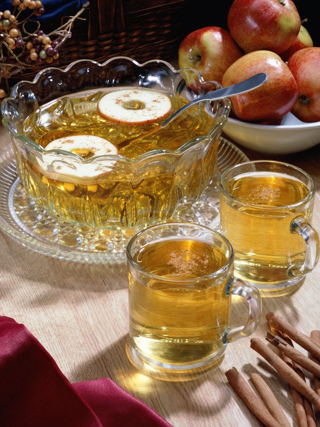 A bowl of apple cider with two glasses and a bowl of apples sitting on a table