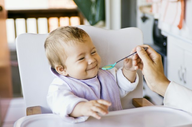 Person spoon feeding baby in high chair