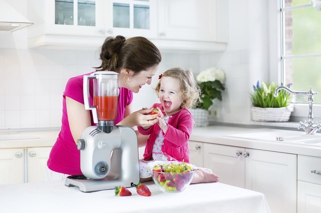 Laughing toddler girl and beautiful mother in sunny white kitchen