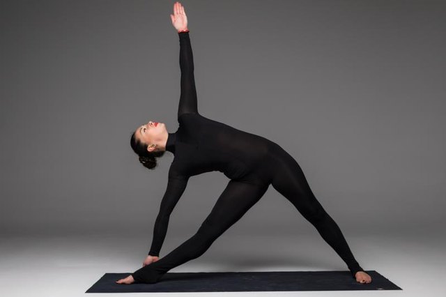 Trikonasana. Beautiful yoga woman practice yoga poses on grey background. Yoga concept.