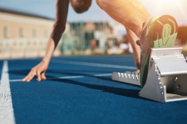 Feet on starting block ready for a spring start. Focus on leg of a athlete about to start a race in stadium with sun flare.