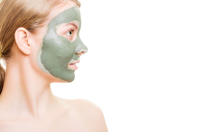 Woman in clay mud mask on face isolated on white.