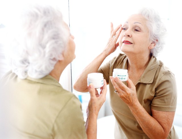 portrait of an elderly woman applying wrinkle cream in the mirror