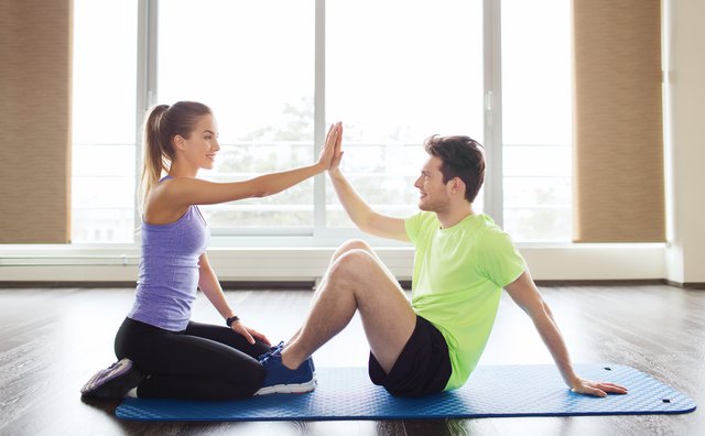 man with personal trainer doing sit ups in gym